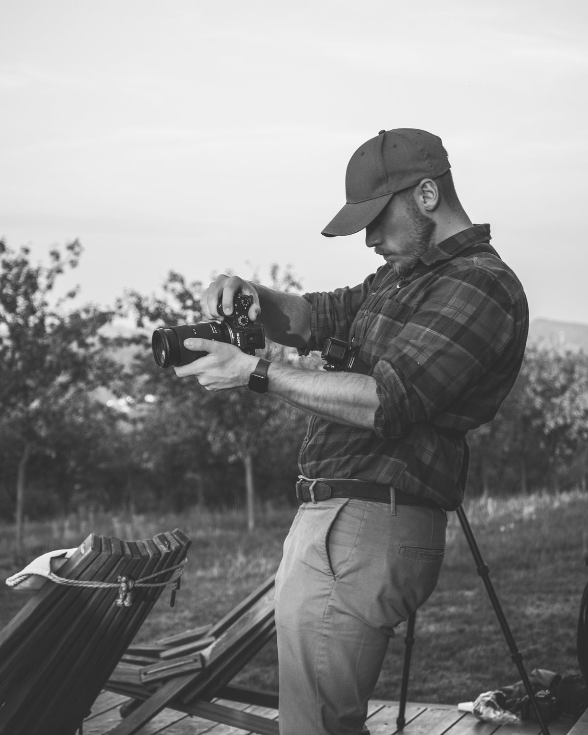Teodor Prchlík v kšiltovce a kostkované košili nastavuje fotoaparát Sony na dřevěné terase u sadu, vedle stativ a dřevěná křesla