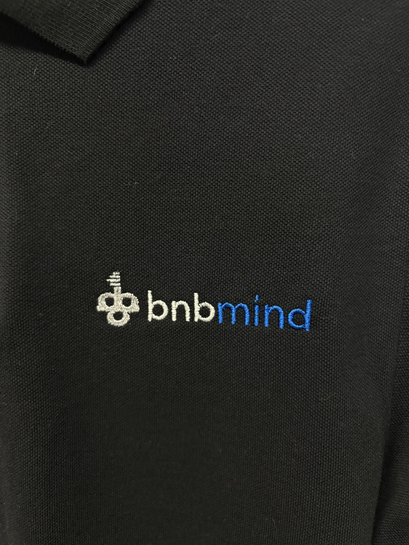 Detail černé polokošile s vyšitým logem BnBMind
