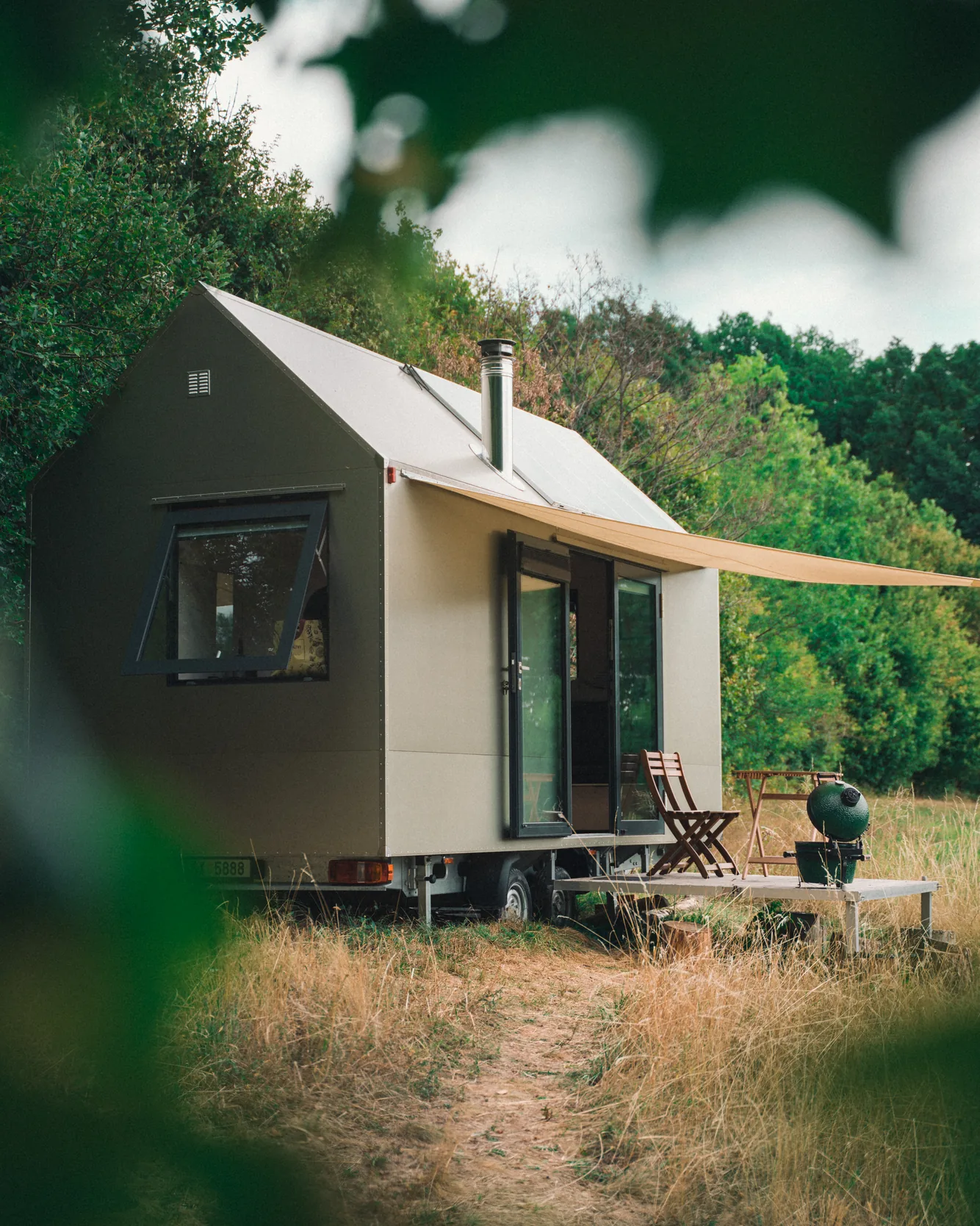 Tiny house s plachtou a terasou, focený přes listy stromu