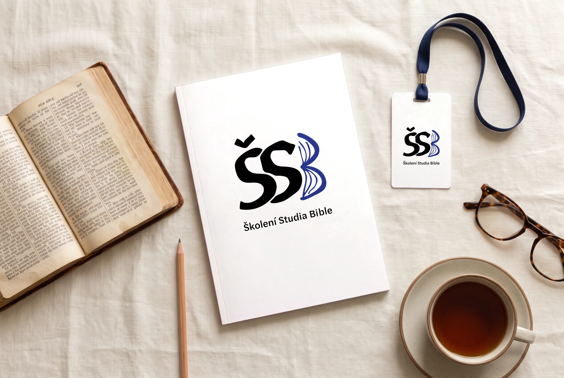 Logo Školení Studia Bible na bílém sešitu a visačce, vedle otevřená Bible, brýle a šálek čaje
